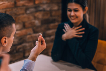 Fototapeta premium Surprised attractive woman getting a marriage proposal from her handsome boyfriend in a restaurant