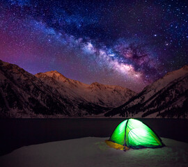 Tent by the lake on a background of snow-capped peaks and the Milky Way at the beginning of the winter season; romantic atmosphere encouraging to travel, explore and discover