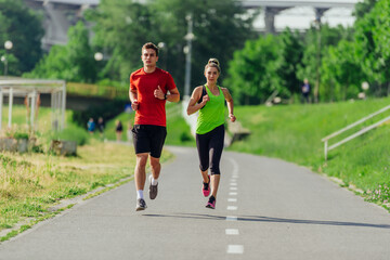 Fototapeta premium Full-length front view of an attractive caucasian couple running together in a park on a sunny day..