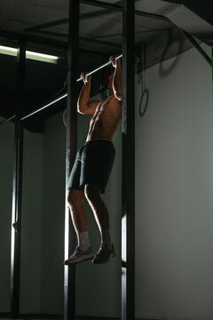 Handsome bodybuilder doing pull-ups on horizontal bar in a indoors modern gym.