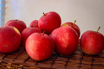 Several ripe red apples stand on a wicker basket illuminated by rays of the sun
