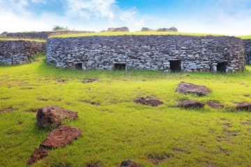 Ruins of the ceremonial village of Orongo, in the archaeological site on the Rano Kau volcano, on Easter Island - Rapa Nui, surrounded by green vegetation, against a blue clear sky.