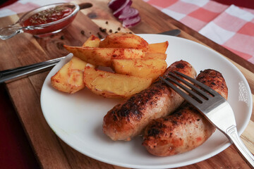 rustic potatoes and grilled sausages lie on a white plate that sits on a cutting board.