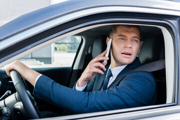 Businessman looking at window while driving car and talking on smartphone.
