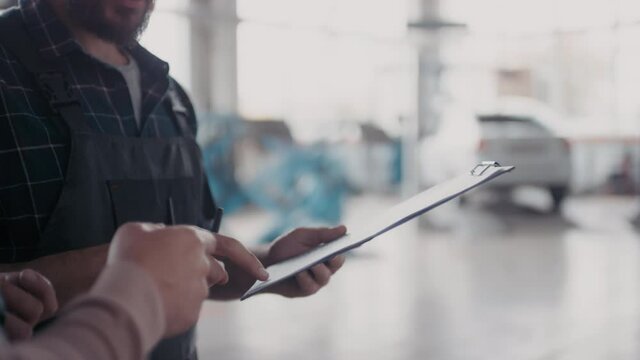 Handheld mid-section of unrecognizable male client signing invoice for services rendered and shaking hands with auto mechanic