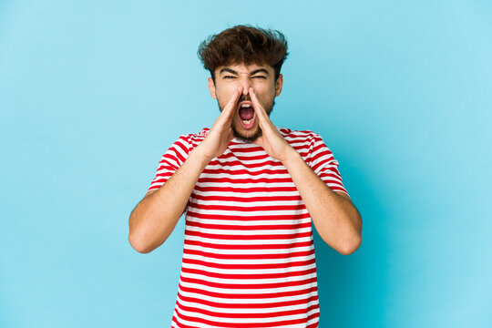 Young arab man on blue background shouting excited to front.