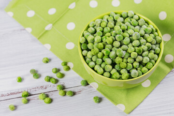Composition with organic frozen vegetables on a white wooden background. Green peas in a bowl.