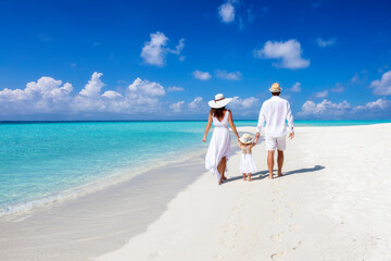 A beautiful family walks together on a tropical paradise beach in the Maldives with turquoise ocean and white sand during their vacation time - 402205670