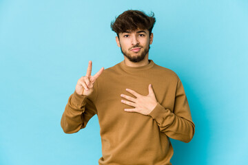 Young arab man on blue background taking an oath, putting hand on chest.