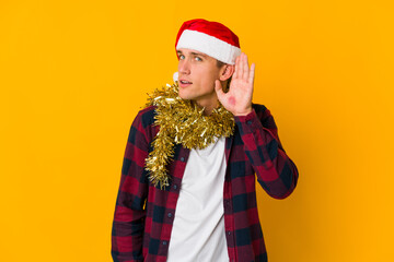 Young caucasian man with christmas hat holding a present isolated on yellow background