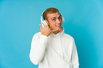 Young caucasian man listening music isolated on blue background