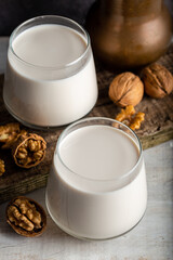 Organic walnut nuts and glass of walnut milk on wooden background.
