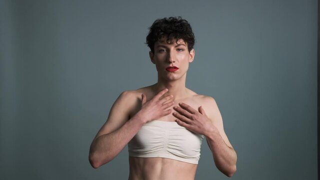 Androgyny. Transgender guy with makeup posing on grey background. Medium shot. Masculine and feminine characteristics in one person. Gender identity concept 4k