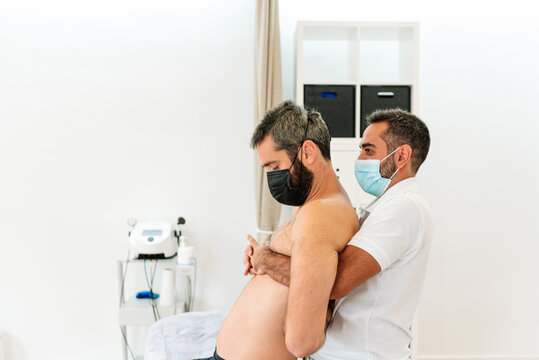 Physiotherapist Stretching The Back Of A Patient With A Serious Injury The Doctor Wearing A Mask Protects Himself From The Covid Pandemic. Concept Of Medicine And Health.