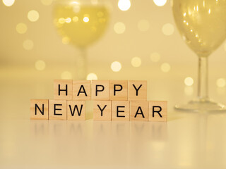 Happy new year - napis z drewnianych kostek, kieliszki szampana w tle 