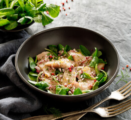Herring salad with lamb's lettuce, chopped onion and herbs in a bowl on a black background close up view