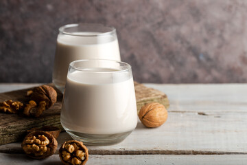 Organic walnut nuts and glass of walnut milk on wooden background.