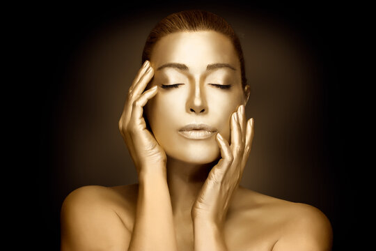 Gold cosmetics. Female model touching golden skin. Gold based beauty treatment