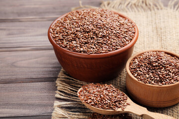 Flax seeds in bowls and spoon on brown wooden background