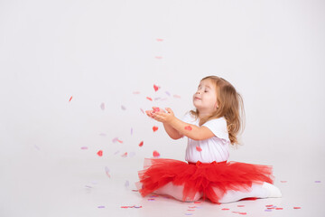 Obraz na płótnie Canvas toddler girl on red skirt throws confetti on a white background.