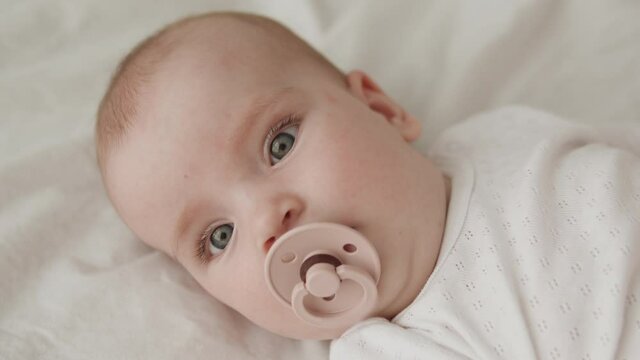 Little green eyed child lying on bed enjoying nipple and looking at camera, love