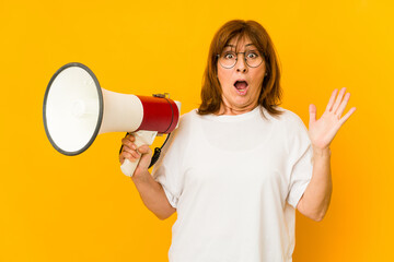 Middle age caucasian woman holding a megaphone surprised and shocked.