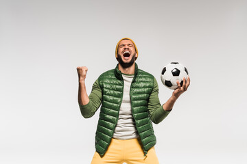 Excited sportsman holding football and showing yes gesture isolated on grey