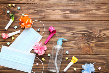 Medical masks with gel sanitizer, whistles, colorful bows and paper stars on brown wooden background