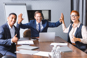 Happy businessman giving high five to multicultural colleagues with thumbs up at workplace in meeting room.