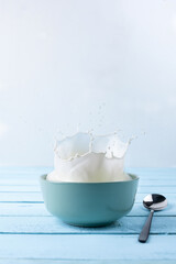 Splash of milk from the dish on a blue wooden background.
