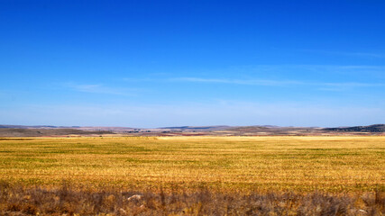 Fototapeta na wymiar Plains of hay fields in summer with gentle hills on the horizon and intense blue sky