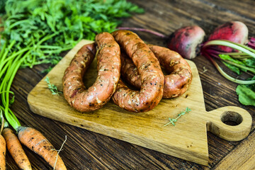 Sausage served on an oak board among vegetables from the home garden. © dominikab