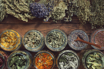 Jars of dry medicinal herbs - calendula, melissa, wild marjoram,  lavender, heather, coneflowers, raspberry and currant leaves, linden tree flowers and bunches of herbs. Top view. - obrazy, fototapety, plakaty