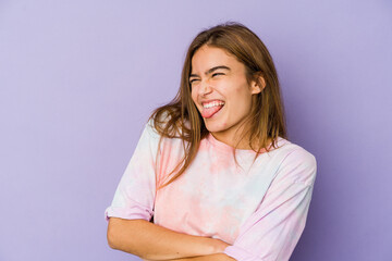 Fototapeta premium Young skinny caucasian girl teenager on purple background funny and friendly sticking out tongue.