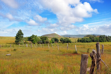 Panoramic view from the slopes of the Terevaka Volcano on Easter Island, showing green vegetation and the ocean against a blue sky.