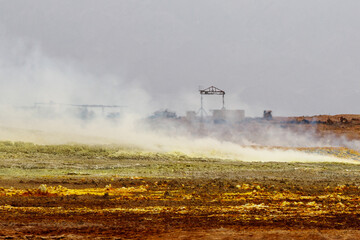 yellow and red stones in a volcanic crater that smoke and boil from the heat, where abandoned sulfur mining buildings remain