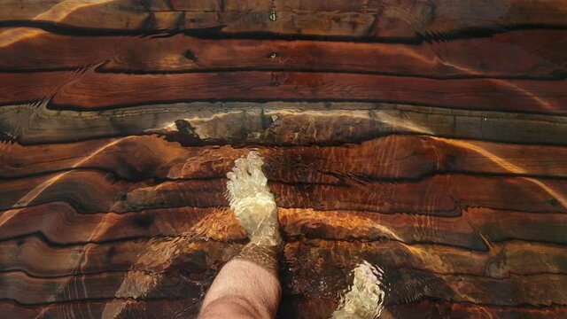 Naked hairy male legs walk on pier. The legs of a man swim. First person of view. Men rest on a flood wood underwater pier. The pavement is covered with water in the lake.