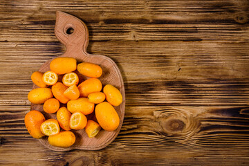 Cutting board with kumquat fruits on wooden table. Top view