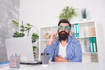 Bearded man in fancy glasses talk on smartphone sitting at desktop in modern office, conversation