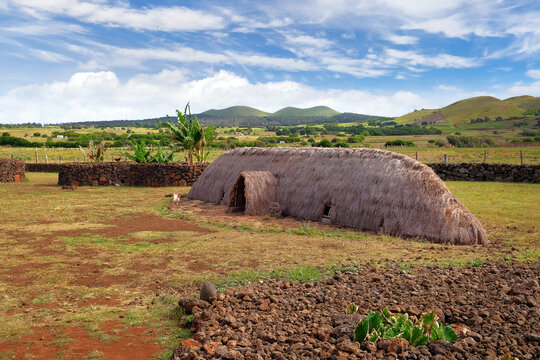 Old Rapa Nui thatch-roofed house at the ceremonial center of Vaihu, on Easer Island, against a blue sky covered by white clouds.