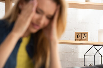 Wooden calendar on shelf with blurred tense woman 