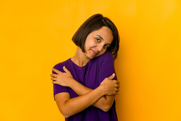 Young hispanic woman isolated on yellow hugs, smiling carefree and happy.