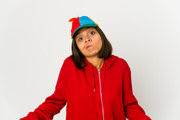 Young hispanic woman wearing a cap with propeller isolated shrugs shoulders and open eyes confused.