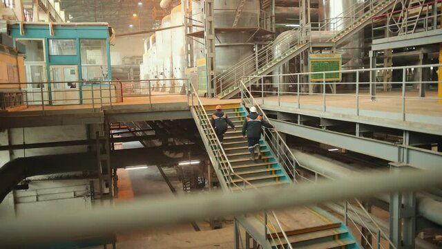 Engineers climb stairs. Rear view. Packing area. Industrial view at oil refinery factory form industry zone. Equipment, cables, piping as found inside of industrial power plant. Manufacturing theme