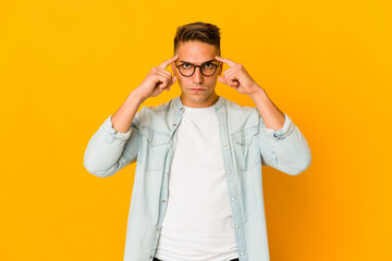 Young handsome caucasian man isolated focused on a task, keeping forefingers pointing head.