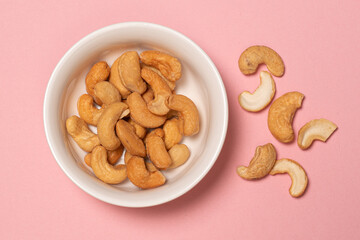 Tasty cashew nuts in bowl on pink background, top view