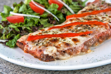 Milanesa a la Nepolitana with lettuce and tomato salad on a plate on a gray granite background