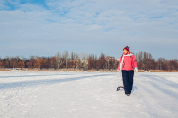 Senior woman carrying sleigh after sledding down. Woman having fun on winter frozen river.