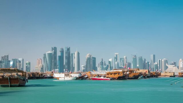 A panoramic view of the old dhow harbour timelapse in Doha, Qatar, with the West Bay skyline in the background. Modern skyscrapers on background and old boats on foreground.