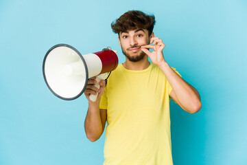 Young arab man holding a megaphone with fingers on lips keeping a secret.